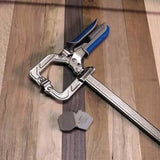 Metal woodworking clamp with blue handle and two clamp pads on wooden surface