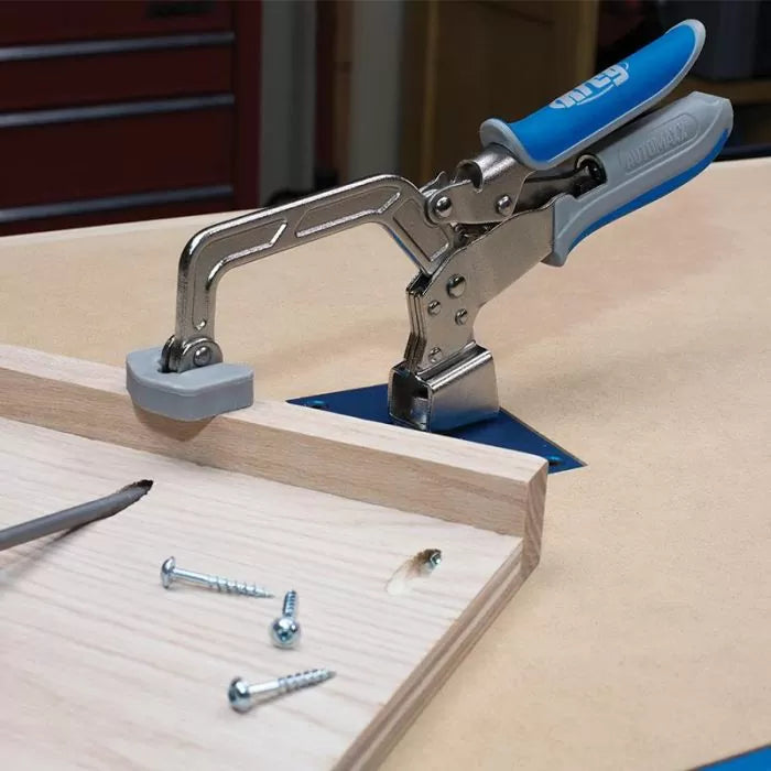 Woodworking bench clamp with blue handles securing a board, screws and pocket hole visible