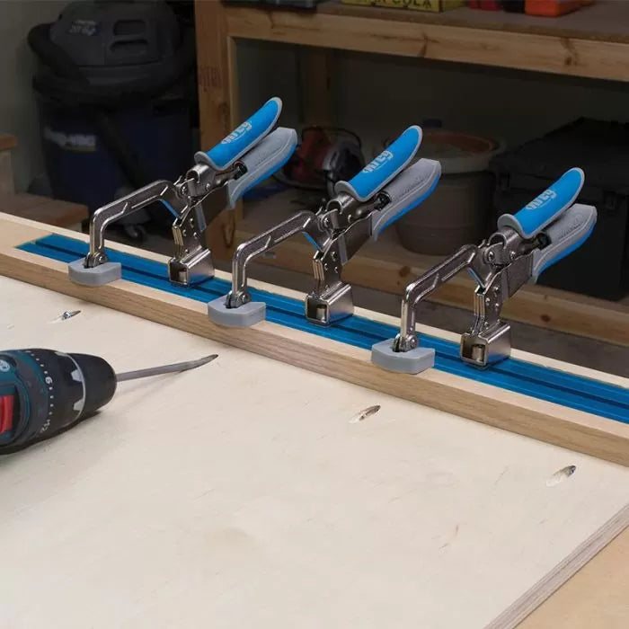 Four toggle clamps mounted on a T-track for woodworking, drill on workbench