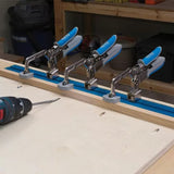 Four toggle clamps mounted on a T-track for woodworking, drill on workbench