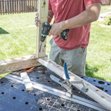 Woodworker using power drill and clamping jig on workbench outdoors for woodworking project