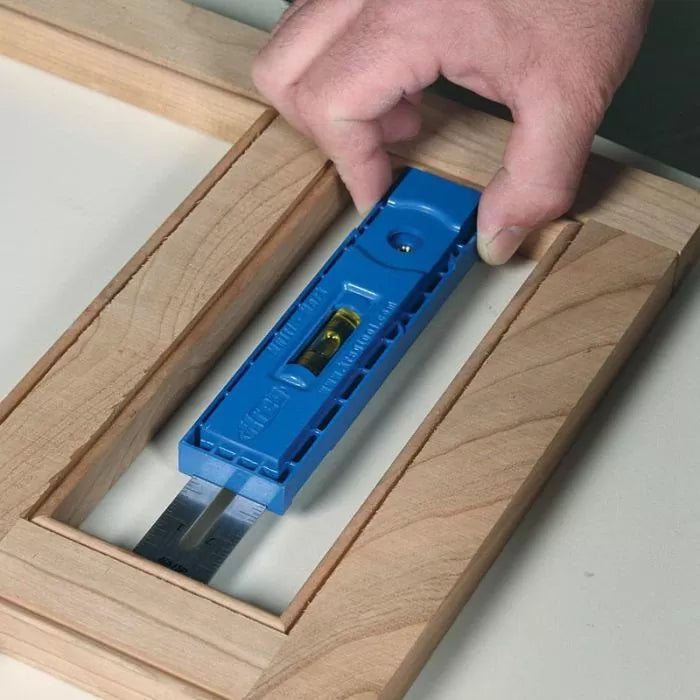 Woodworker using blue marking gauge and level tool to align frame joints on wood project