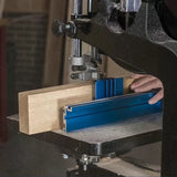 Woodworker guiding a board through a bandsaw with precision blue fence in a workshop.