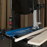 Bandsaw cutting wood with blue fence in woodworking shop, precision saw accessory in use