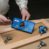 Person using Kreg cabinet hardware jig with screwdriver on wooden cabinet door, router bit nearby