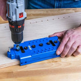 Drill being used with blue woodworking dowel jig on wooden board for precise hole placement