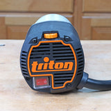Close-up of a Triton woodworking router power tool on a workbench in a workshop setting.