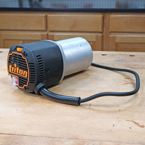 Triton router motor with power cord on a woodworking bench in a workshop setting