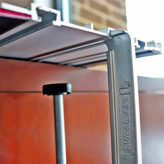Metal woodworking clamp securing a tabletop, featuring a threaded screw and sturdy frame.