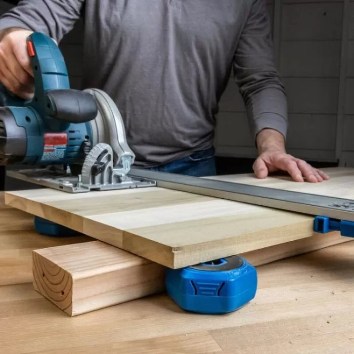 Woodworker using a circular saw with a guide rail to cut a wooden board on a workbench
