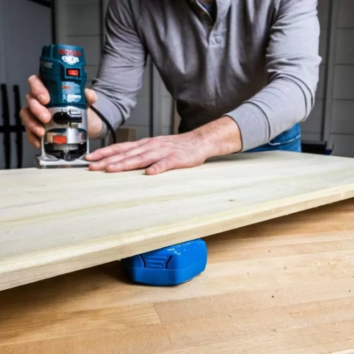 Person using a handheld router on wood supported by a non-slip workbench riser