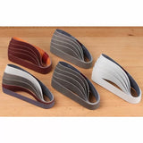 Assorted sanding belts for woodworking on a wooden surface, multiple grits and colors