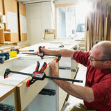Woodworker using quick-release bar clamps to assemble cabinets in a bright workshop