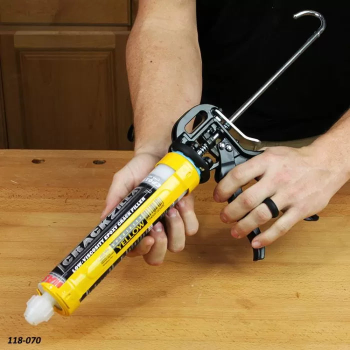 Person using a manual caulking gun with epoxy crack filler on a woodworking bench
