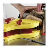 Yellow featherboard holding wood on a bandsaw table during woodworking