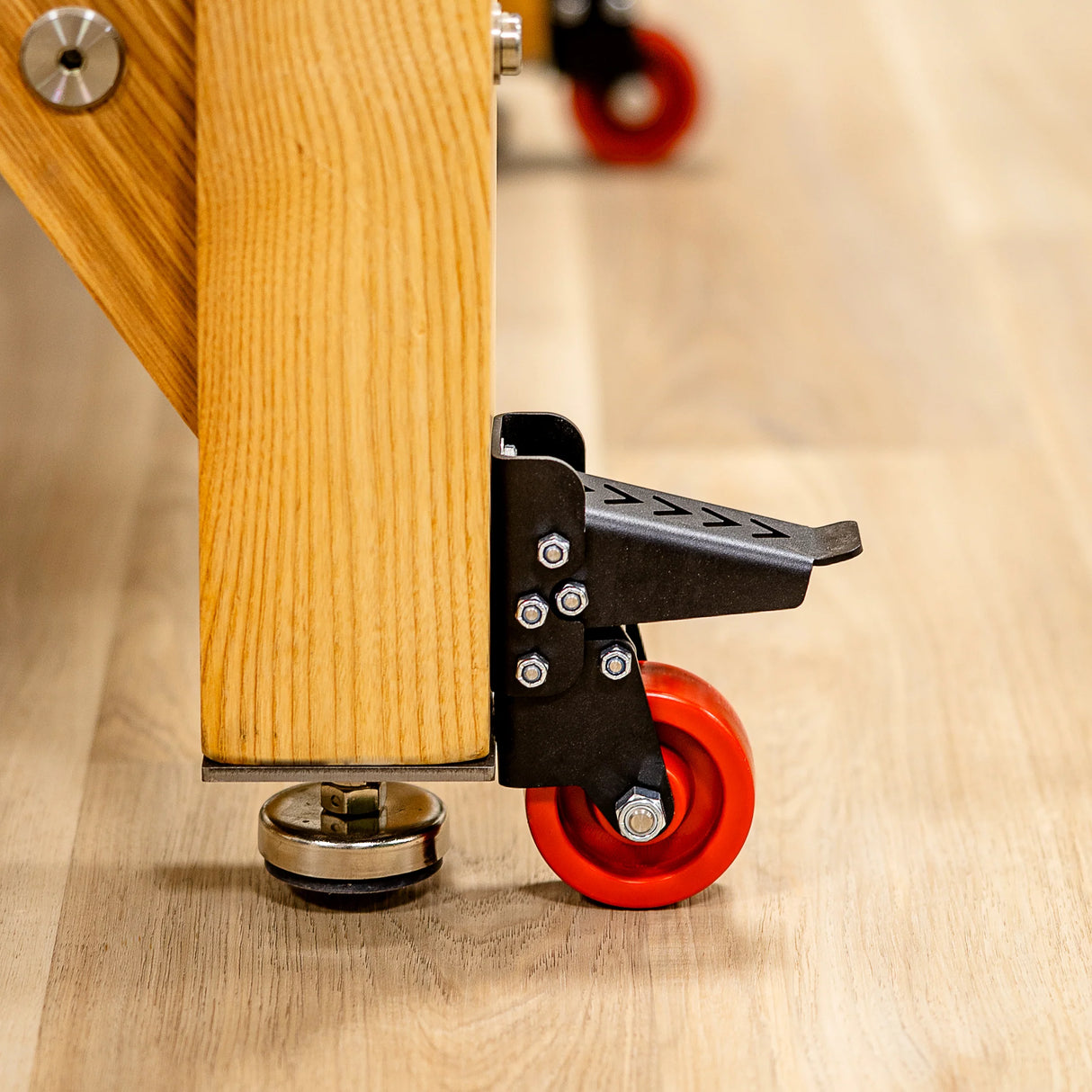 Workbench caster wheel with red polyurethane wheel and black foot pedal on wood floor