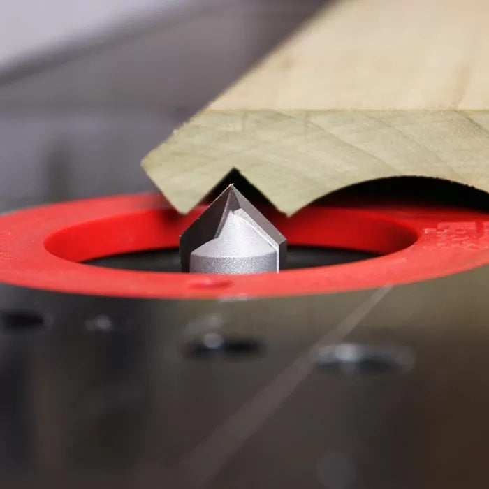 Router table with V-groove router bit cutting angled groove in wood, woodworking tool closeup