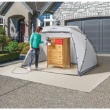 Woman using paint sprayer on wooden dresser inside portable spray shelter outdoors