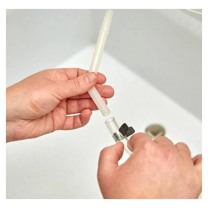 Hands connecting a plastic tube to a small valve over a white sink.
