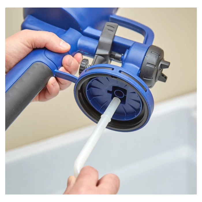 Person cleaning or assembling a blue handheld paint sprayer with a plastic tube