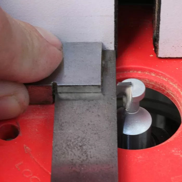 Woodworker setting router bit height using metal gauge on red router table