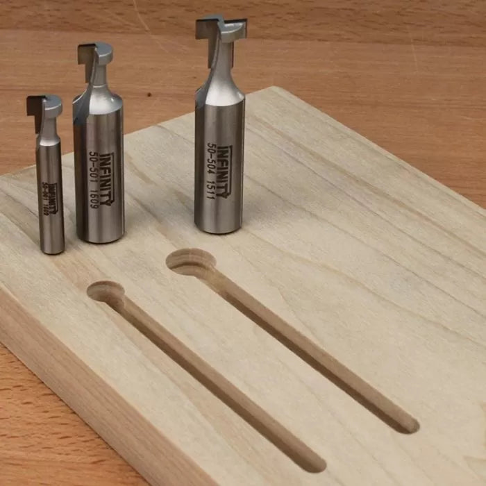 Set of metal router bits next to a wooden board with T-slot grooves on a workbench