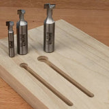 Set of metal router bits next to a wooden board with T-slot grooves on a workbench