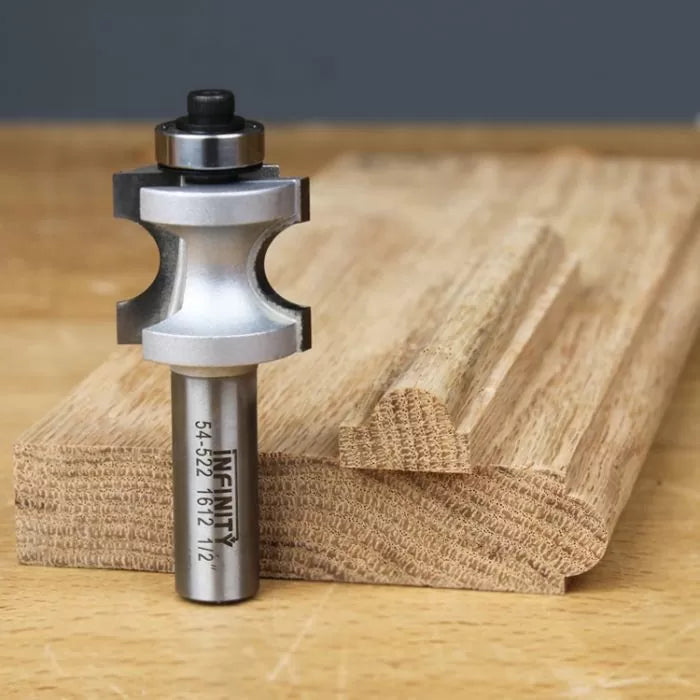 Roundover beading router bit with bearing next to decorative wood trim sample on workbench