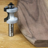 Roundover router bit with bearing next to a smoothly edged wooden board on workbench
