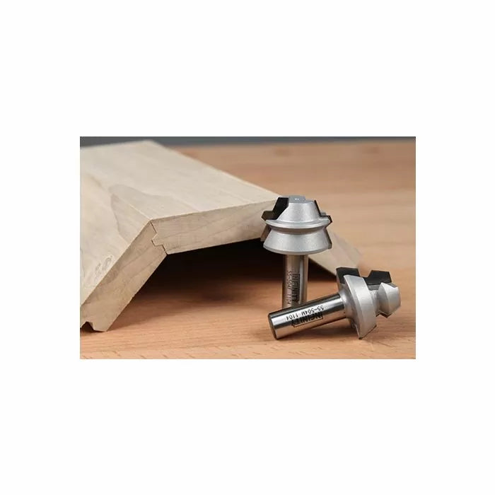 Two woodworking router bits next to a shaped wooden board on a workbench