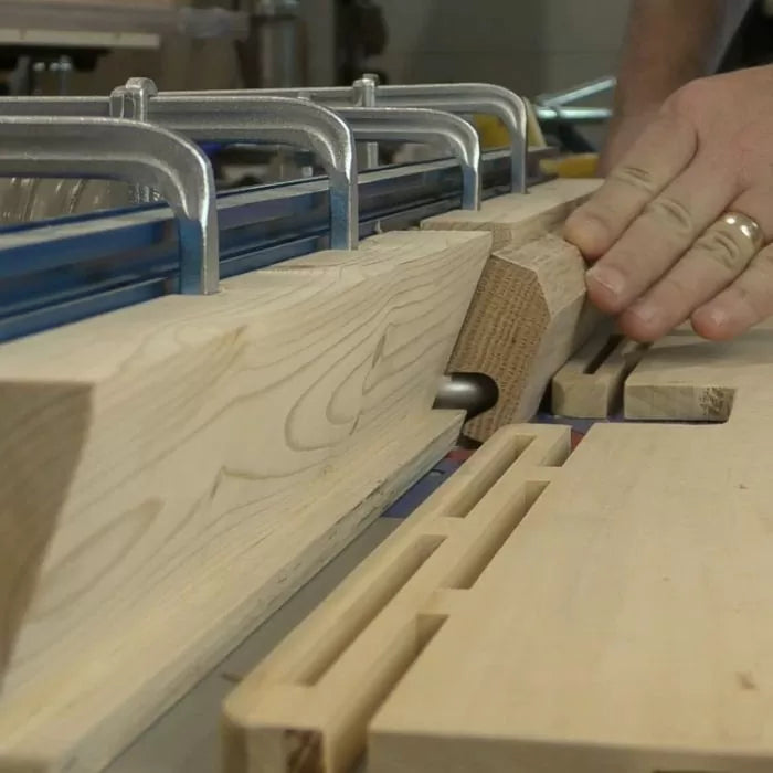 Woodworker using a router table to mill precise slots in hardwood board