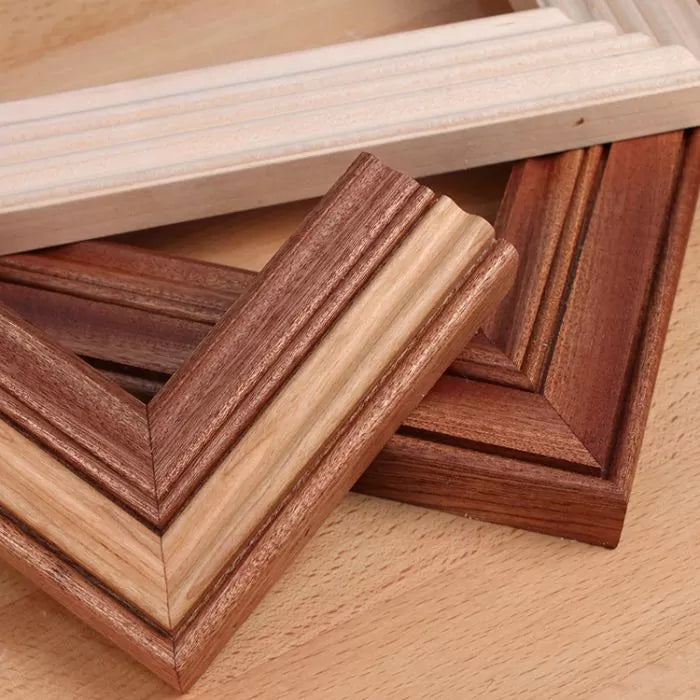 Assorted wooden picture frame moldings with detailed profiles on a wood surface.
