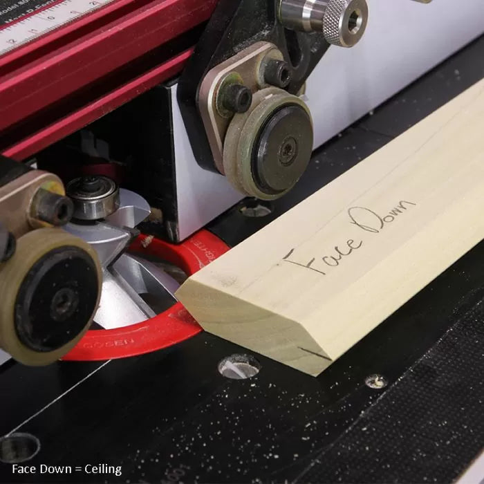 Router table setup cutting crown molding with a labeled wood piece and red router bit visible.