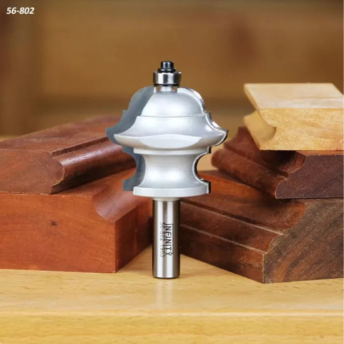 Crown molding router bit for woodworking with sample decorative wood profiles on a workshop table.