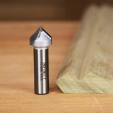 Carbide router bit with sharp angled tip on wood surface beside a beveled wooden board