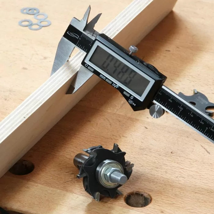 Digital caliper measuring wood thickness, router bit and washers on workbench, woodworking tools