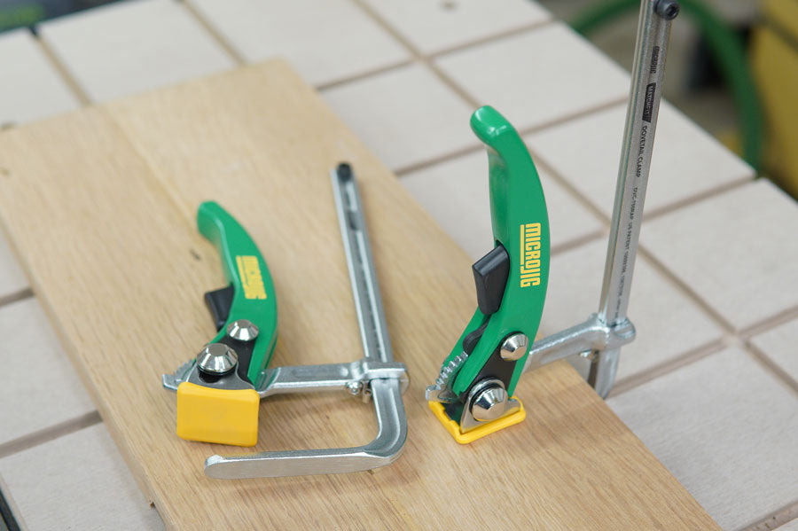 Two green toggle clamps securing a wooden board on a workbench, woodworking tools