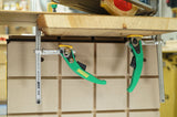 Workbench with two green lever woodworking clamps securing a wooden board