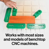 CNC clamping kit with green hold-down clamps securing wood on a benchtop CNC machine.
