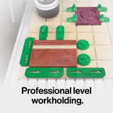 CNC workholding kit with green clamps and wooden workpiece on a grid table, woodworking tools