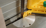 Close-up of a bandsaw blade with yellow safety jig and fence on a metal table saw surface