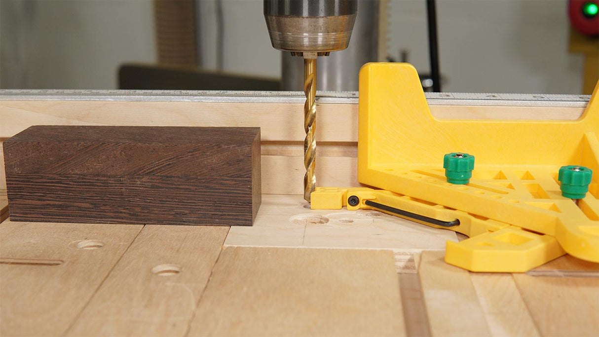 Drill press making precise hole in wood block with yellow woodworking jig on tabletop