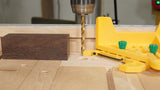 Drill press making precise hole in wood block with yellow woodworking jig on tabletop