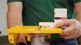 Person measuring router bit height with setup gauge on yellow router table