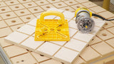 Woodworking router tool and yellow push block on CNC work table with MDF grid and holes