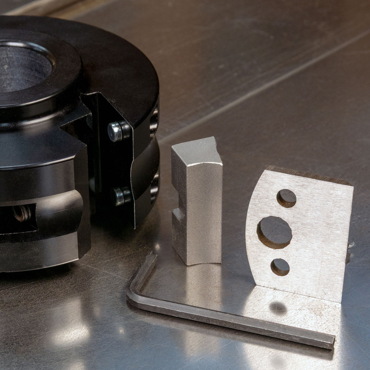 Shaper cutter head attachment with metal woodworking blades and hex key on a table saw surface.