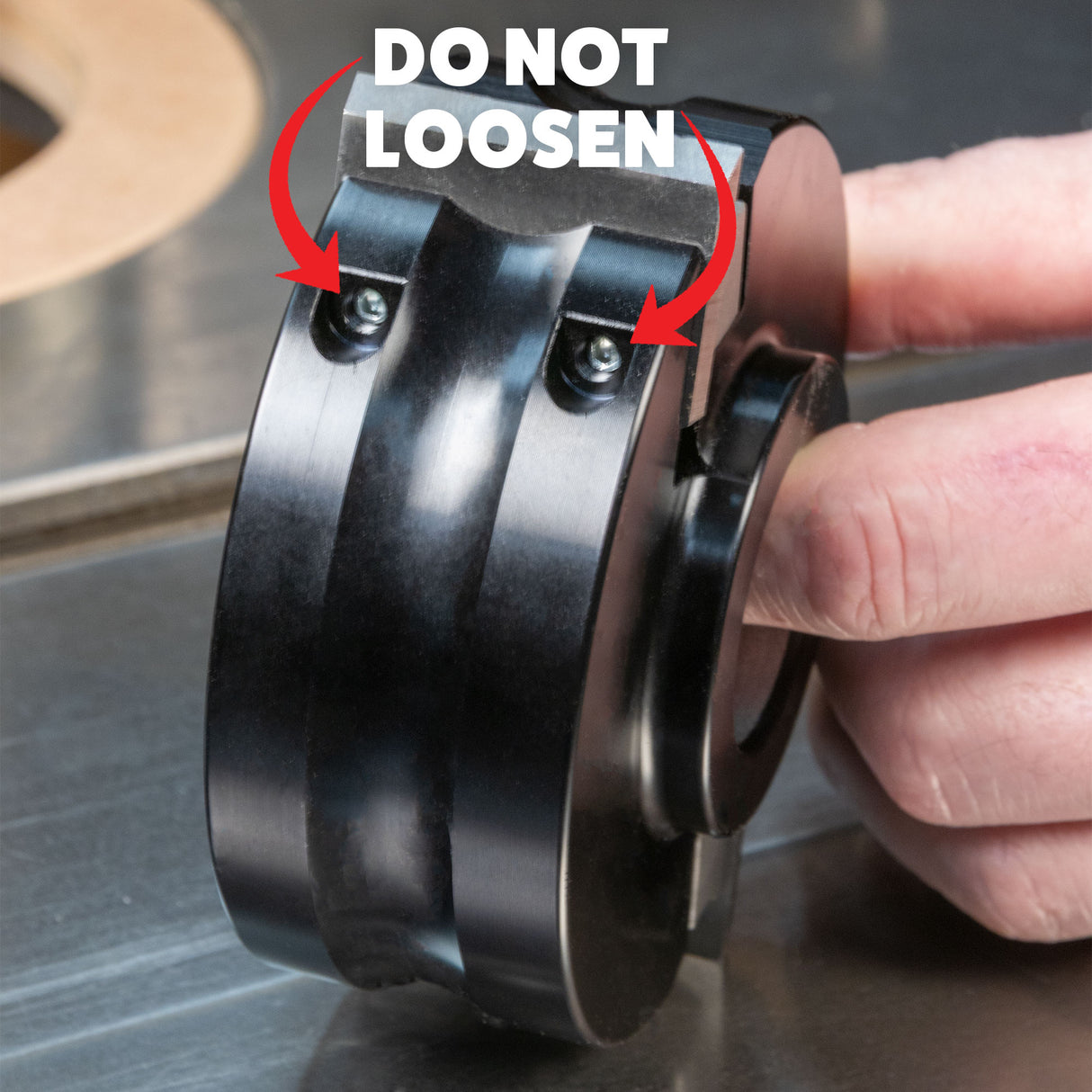 Hand holding a woodworking shaper cutter with screws labeled 'DO NOT LOOSEN' for safety