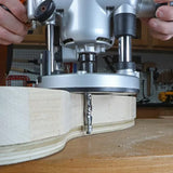 Handheld plunge router cutting curved edge on plywood in woodworking shop
