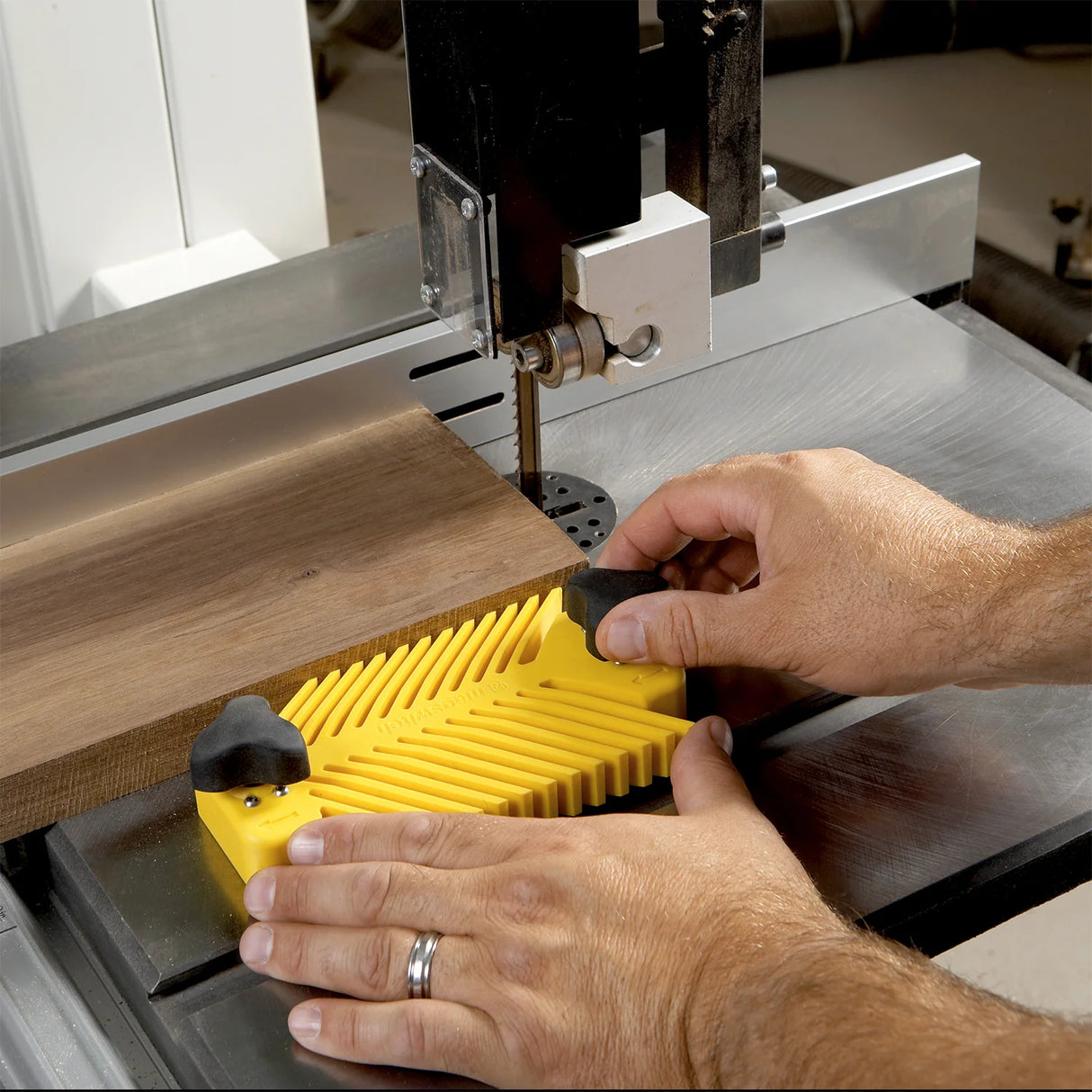 Woodworker using yellow featherboard on band saw for precise woodworking cut