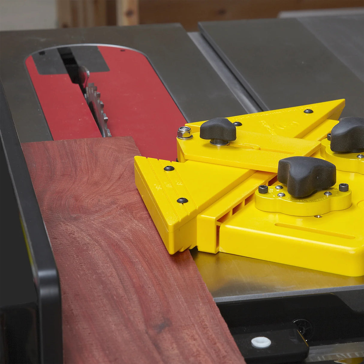Yellow table saw push block guiding wood on a table saw with exposed saw blade.